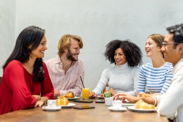 group of multi ethnic fiends having breakfast, focus on the blonde man and the afro hair woman, table with coffee, cappuccino, orange juice and pastry, university students pause in a cafeteria 