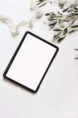 Electronic device mock-up. Closeup of tablet with empty screen. Olive tree branches and silk ribbon...