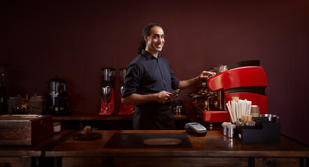 Portrait of a handsome barista in black shirt and apron at the bar of the modern cafe.