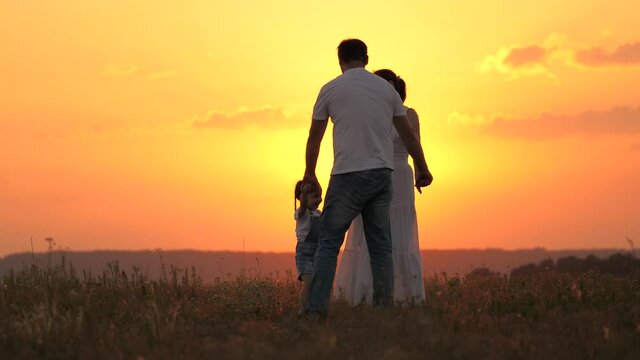 Happy family walk, silhouette of mom and dad baby at sunset. Dad, daughter and mom are walking holding hands in park. Happy childhood and dreams. Parents and cheerful child are dancing in park in sun