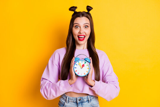 Photo of young happy excited cheerful shocked amazed girl smiling hold clock isolated on yellow color background