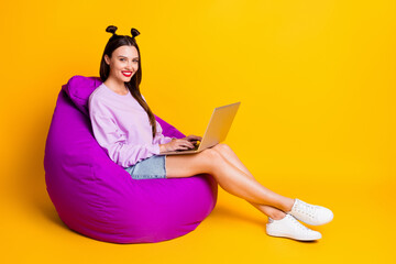 Full size photo of young cheerful positive good mood girl sit armchair studying in laptop isolated on yellow color background