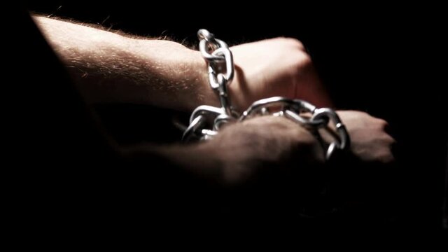 Adult man hands chained with metal chain against his will