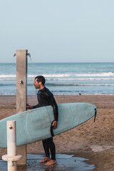 Male wearing a neoprene suit holding a surf board