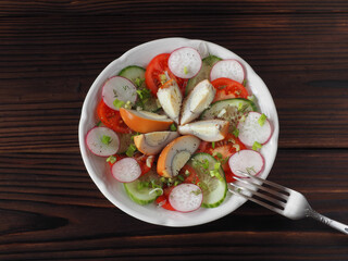 Slices of smoked egg, tomatoes, cucumber, radish with green onions and spices in a plate, fork on a dark wooden table, flat layout. Recipe for vitamin salad with chicken eggs