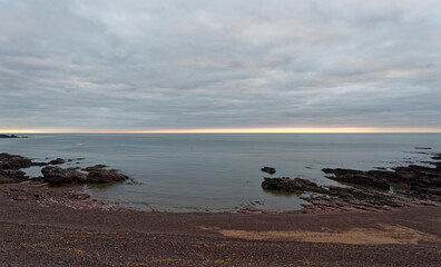 The mixed sand and shingle beach at low tide beneath the cliffs of the Scottish Fishing Village of Auchmithie on the East Coast of Scotland.