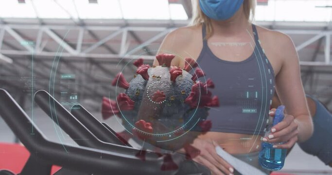 Animation of covid 19 cell over woman in face mask wiping equipment in gym