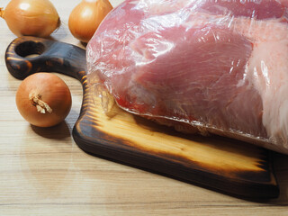 Fresh pork in vacuum packaging on the kitchen board, onions on the table. Natural raw meat is...