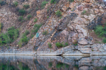 Rocky shore abandoned quarry, slope with sparse bushes near the lake