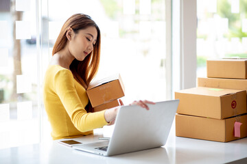 Person preparing online store orders for shipping using box and laptop