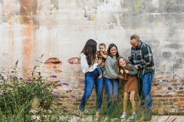 A family of five with two girls and a baby boy standing by an urban old brick wall