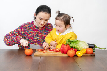Fototapeta premium Mother and girl are tidying up vegetables in the kitchen