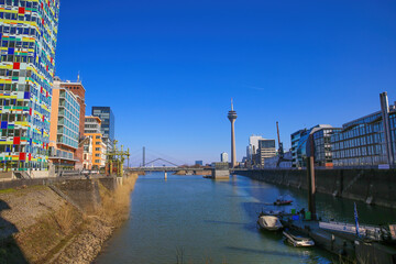 Obraz premium Düsseldorf, Germany - March 1. 2021: View over water canal beyond modern buildings on rhine tower against blue sky