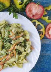 Pasta with vegetables and cheese in a white plate on a blue wooden background
