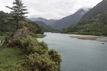 Beautiful view of the flowing river surrounded by mountains covered in greens under the cloudy sky