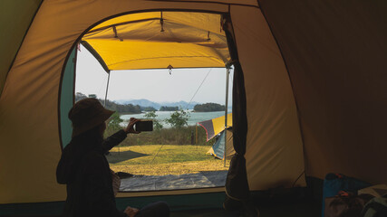 A female Asian tourist sits in a tent taking photos of the beautiful nature views with their mobile phones.