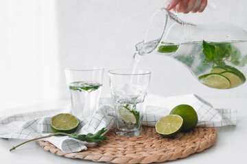 Detox water with lime fruit. Hand pouring lime fruit water from jug into glasses