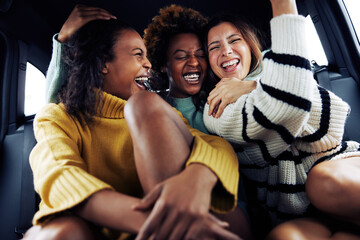 Laughing group of diverse female friends riding together in a car