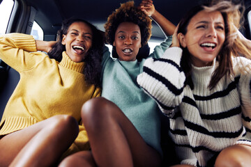 Carefree young friends laughing in the backseat of a care