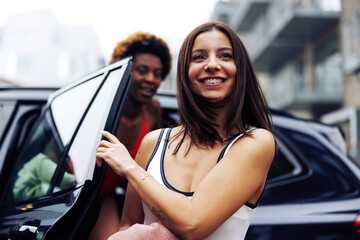 Smiling female friends in a swimwear getting out of a car