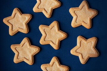 Fototapeta na wymiar Top view of delicious gingerbread cakes in the shape of stars lying on a blue background, depicting the night starry sky. Holiday.