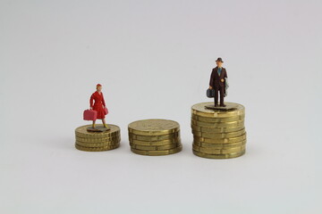 zwei kleine Figuren Frau und Mann stehen auf unterschiedlich hohen Stapeln aus Münzen steht für...