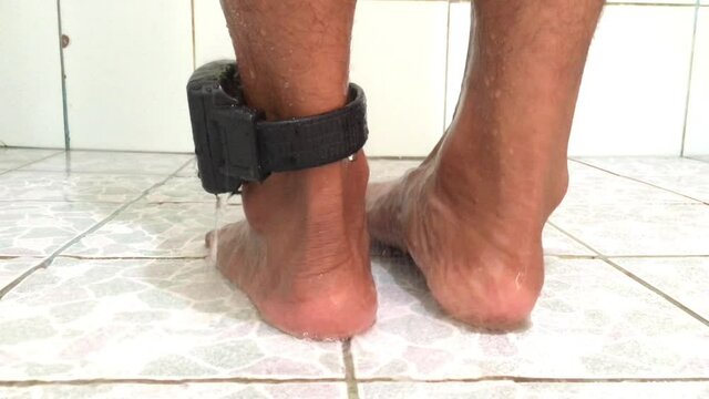 A male prisoner taking a shower In the bathroom there are white tiles. With a Electronic Monitoring (EM) to the leg Waterproof, no short circuit.