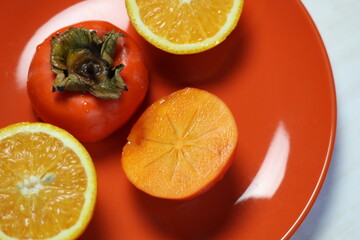 fresh orange fruit and persimmon halfs on orange plate 