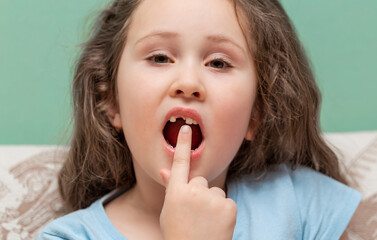 Naklejka premium The little girl has no tooth. The child lost a baby tooth. The baby shows the place where the tooth fell out. High quality photos