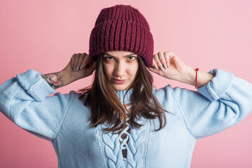 Portrait of a brunette girl in a warm hat in the studio on a pink background