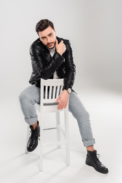 Bearded stylish man sitting on shite chair on grey background