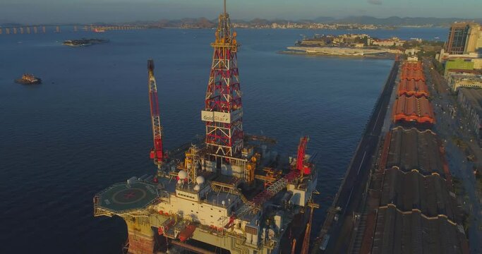 Aerial around industrial oil rig platform revealing city of Rio de Janeiro behind on sunny afternoon
