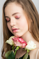 Little pretty girl in pink holds the bouquet of roses. Close up the flowers and face. Beautiful little girl with flowers