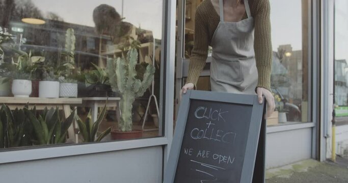 Small business retail owner opening store with click and collect, curb-side pickup sign during coronavirus pandemic