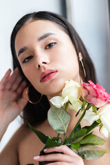 young beautiful woman smelling a bunch of red roses. fashion interior photo of beautiful smiling woman with dark hair holding a big bouquet of red roses in Valentine's day