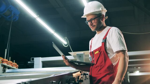 Maintenance man with a laptop is observing a rolling conveyor