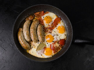 Pan-fried sausages and eggs. View from above. Studio photo on black background