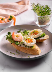 Breakfast with bruschetta with shrimps, eggs and microgreens in a plate