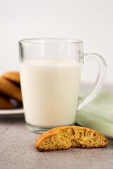 Blurred image of half a cookie in the foreground, a glass cup with milk and a cookie in a white plate.