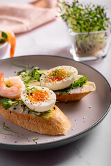 Breakfast with bruschetta with shrimps, eggs and microgreens in a plate