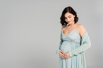 Smiling pregnant woman looking at belly isolated on grey