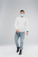 Stylish man in medical mask walking on grey background