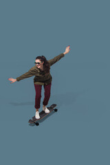 Obraz premium Skateboarding. High angle view of young woman on blue studio background. Girl in motion. Human emotions and facial expressions concept. Full length portait, copyspace for ad. Fashion, retro style.