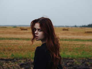 Fototapeta premium Portrait of a red-haired woman in a black dress in a field in nature cropped view
