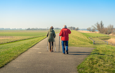 Nordic walkers on the top of a Dutch dike take a break because the man is on the phone with his...