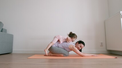 Mother does exercise and little girl climbs over mother's back at home