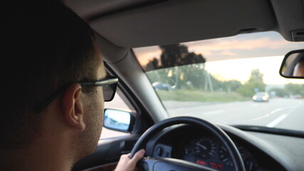 Unrecognizable man in sunglasses driving car on highway. Young confident guy looking to road during controlling auto. Back view from vehicle salon. Concept of road trip. Slow motion