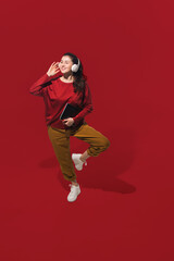 Fototapeta na wymiar Dancing with headphones. High angle view of young woman on red studio background. Human emotions and facial expressions concept. Full length portait, copyspace for ad. Fashion, retro style.