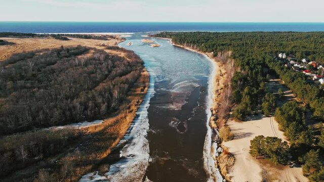 Flight up: Spring aerial view over river joining Baltic sea with melting ice and snow