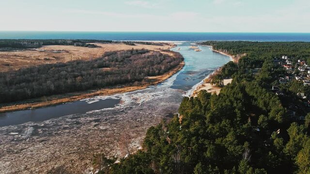 Flight forward: Spring aerial view over river joining Baltic sea with melting ice and snow